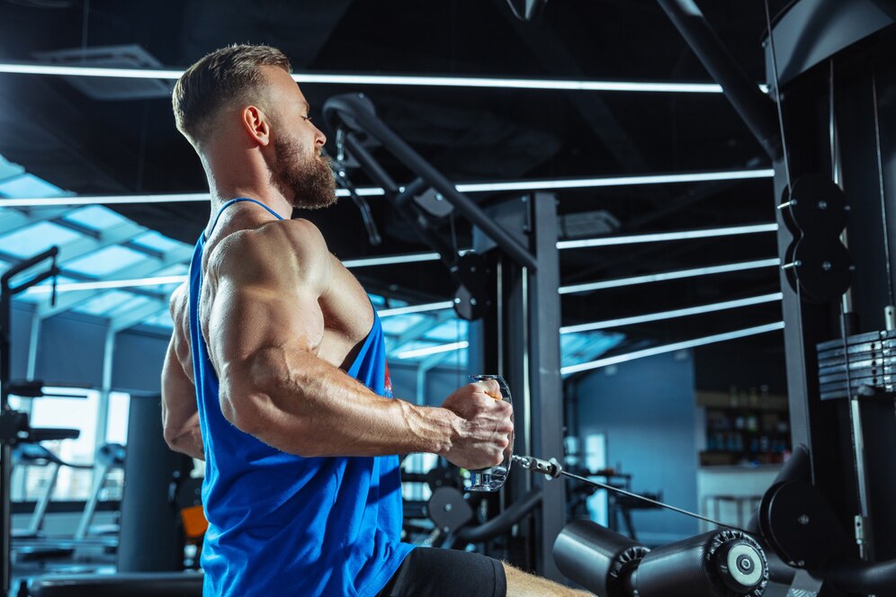 A muscular man in a blue tank top using a rowing machine in a modern gym.