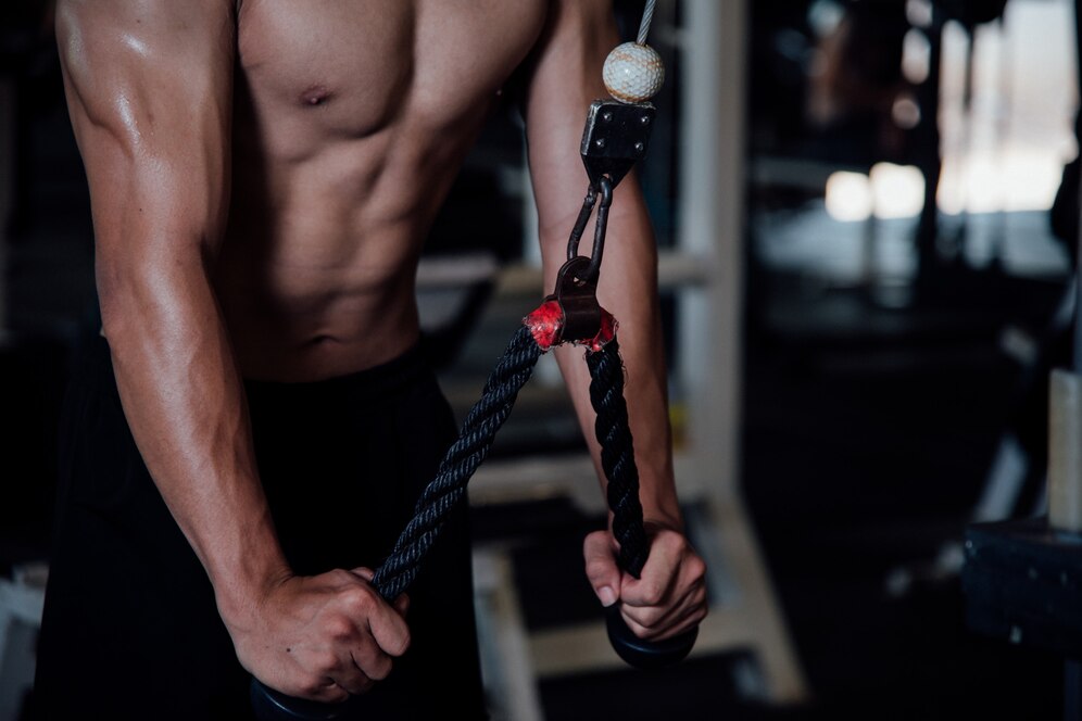 man with a toned abdomen using a cable machine at a gym.