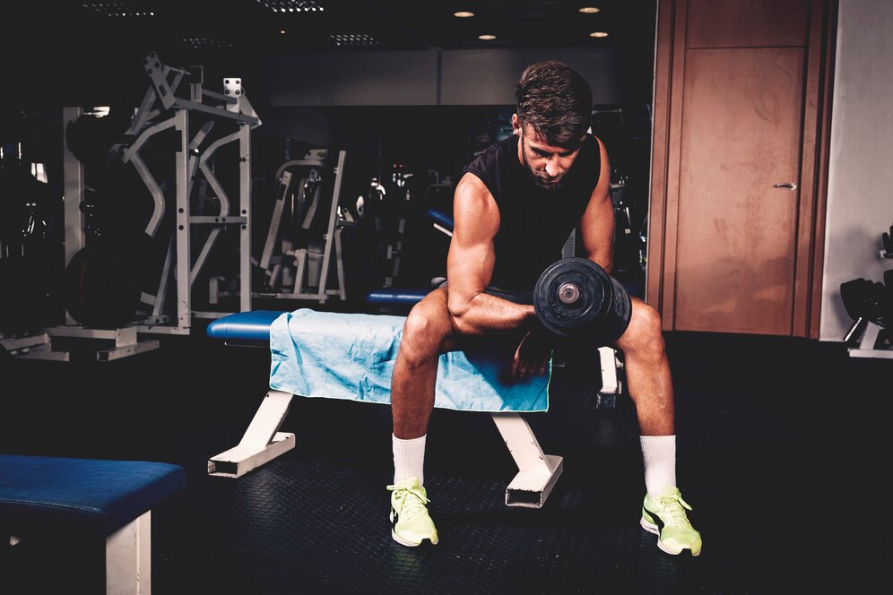 Man lifting dumbbell while seated on a bench in a gym.